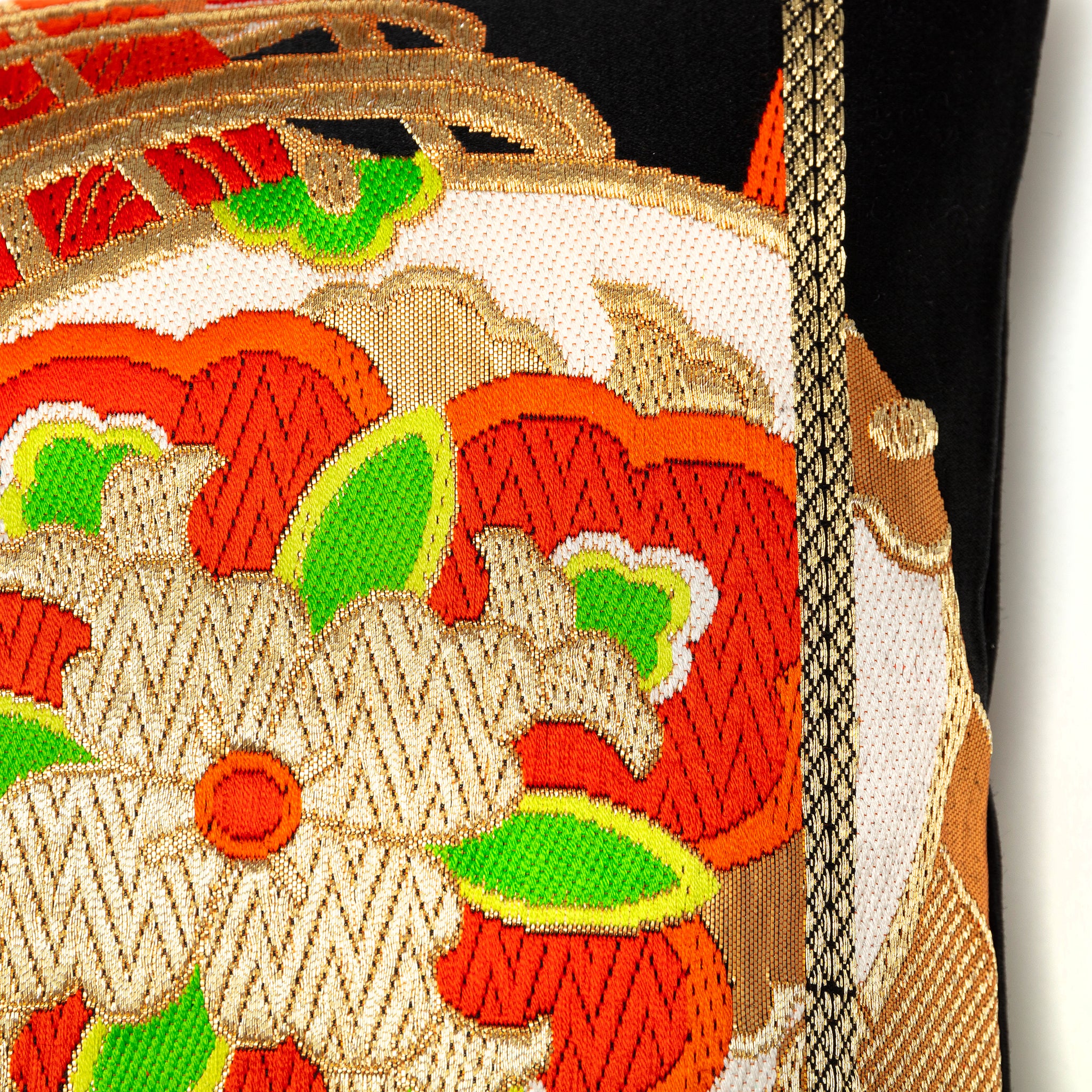 Close-up of the Golden Drum Obi Pillow’s textured black silk fabric with vibrant orange and green embroidered accents along