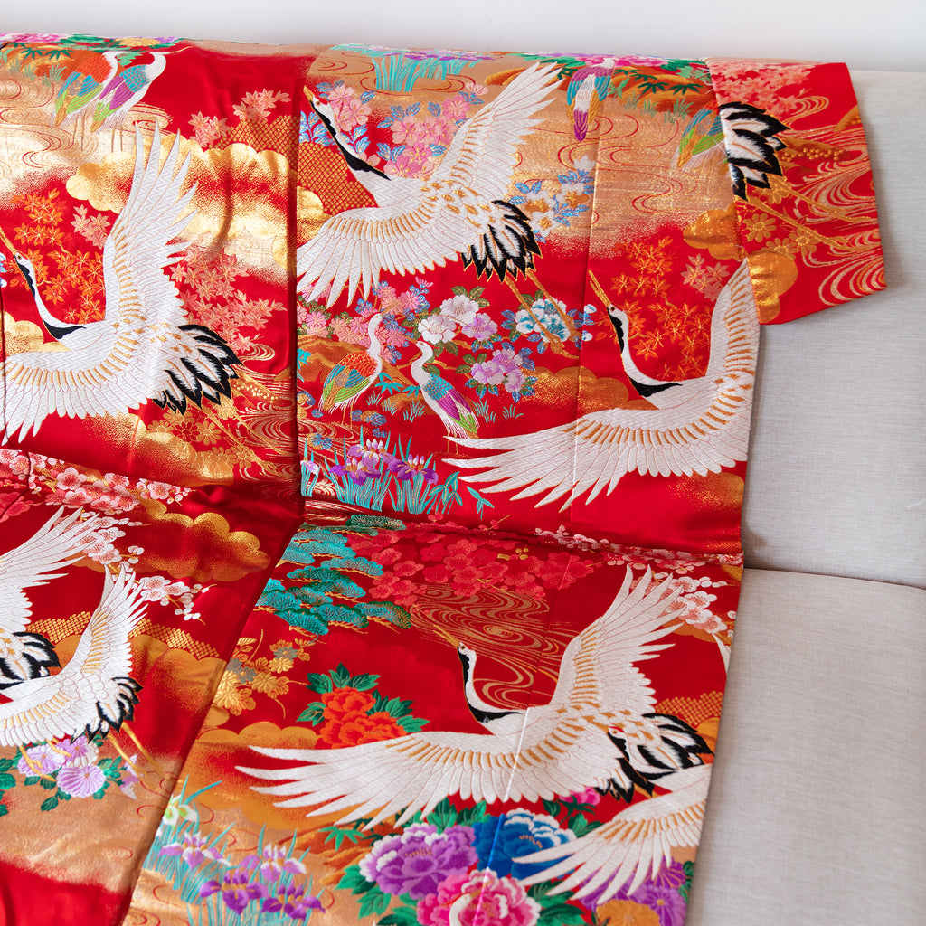 Close-up of the textured silk fabric showcasing intricate vintage floral embroidery on the red kimono bedspread edge.