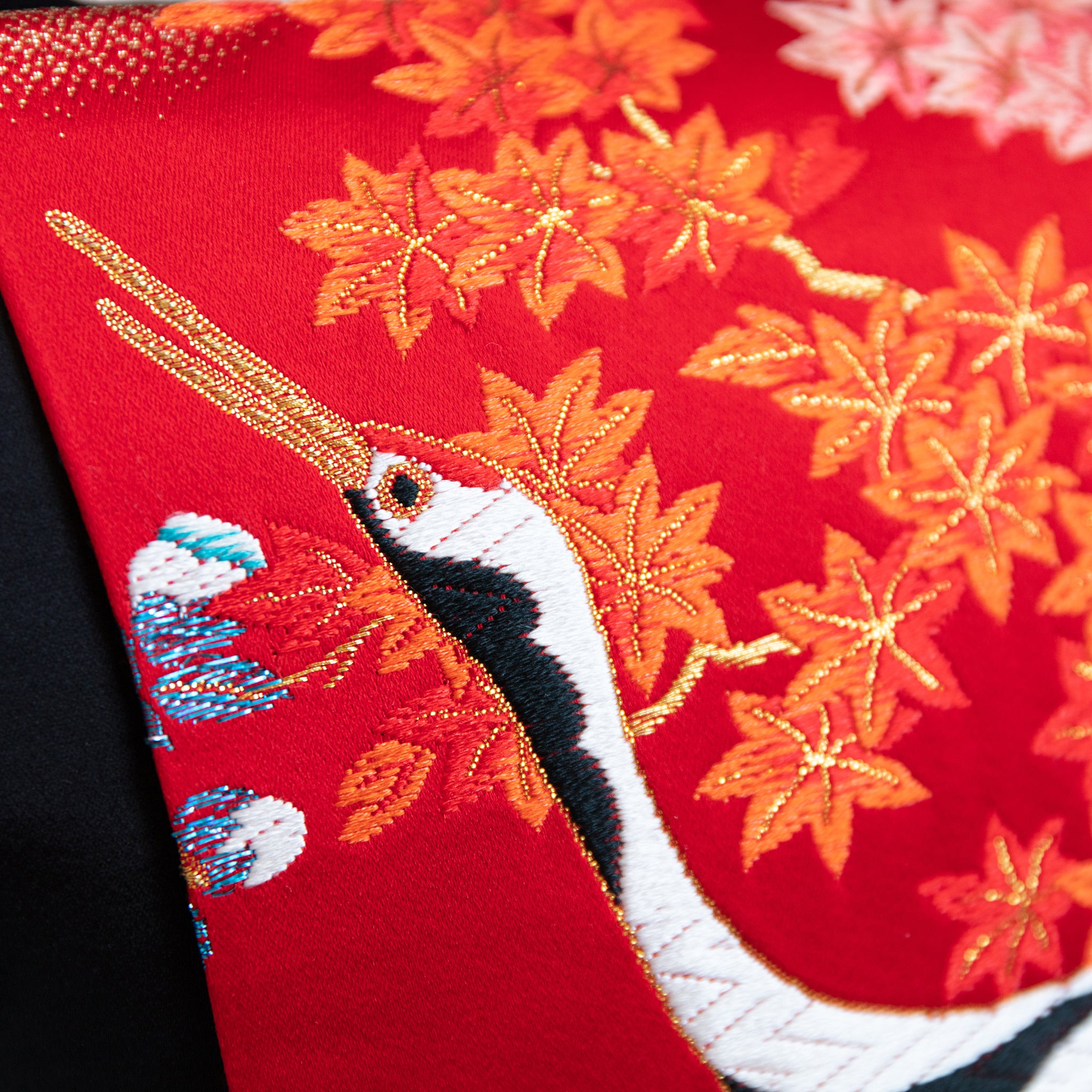 Close-up of red silk embroidered cranes detail on black velvet surface, highlighting intricate stitching and rich texture.