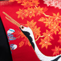Close up of an embroidered birds head and beak over red silk flowers, part of a japanese obi pillow.