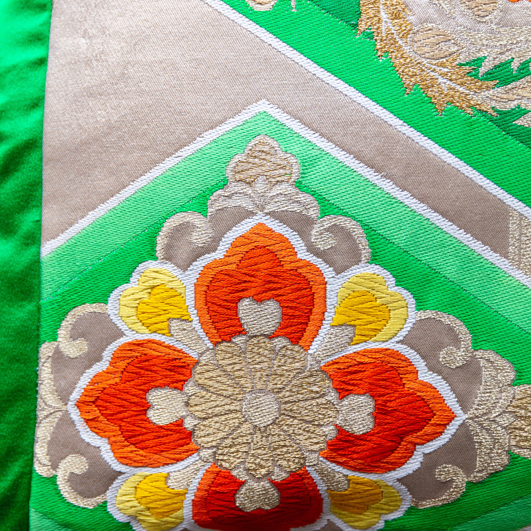 Close-up of the golden phoenix embroidery detail on the green silk obi cushion’s textured gold velvet surface showing